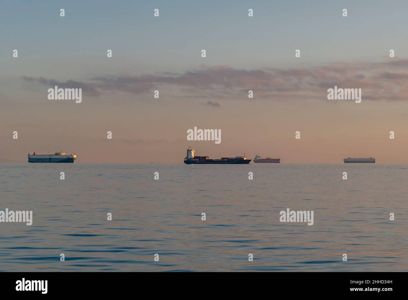 Cuatro grandes barcos de contenedores navegan en la línea del horizonte a la luz del atardecer Foto de stock