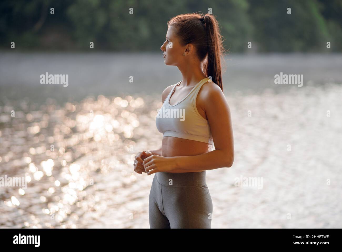 De cerca hermosa mujer morena en elegante ropa deportiva de pie en el  muelle cerca del lago y verde bosque en el fondo. Soleado día de verano  Fotografía de stock - Alamy