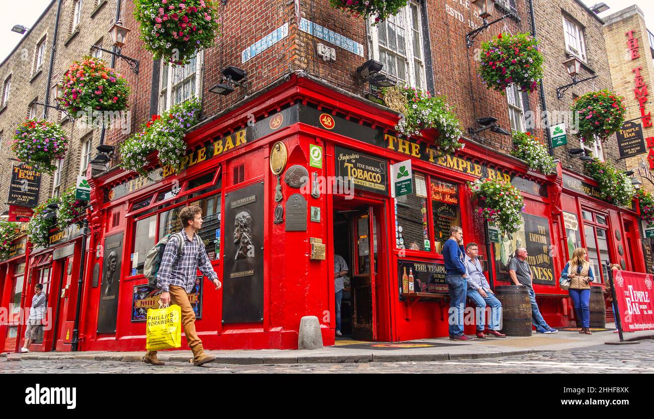 Ein junger Mann mit einer Einkaufstüte geht an der Temple Bar en Dublin vorbei und blickt auf eine Gruppe Jugendlicher, die an dem Gebäude stehen Foto de stock