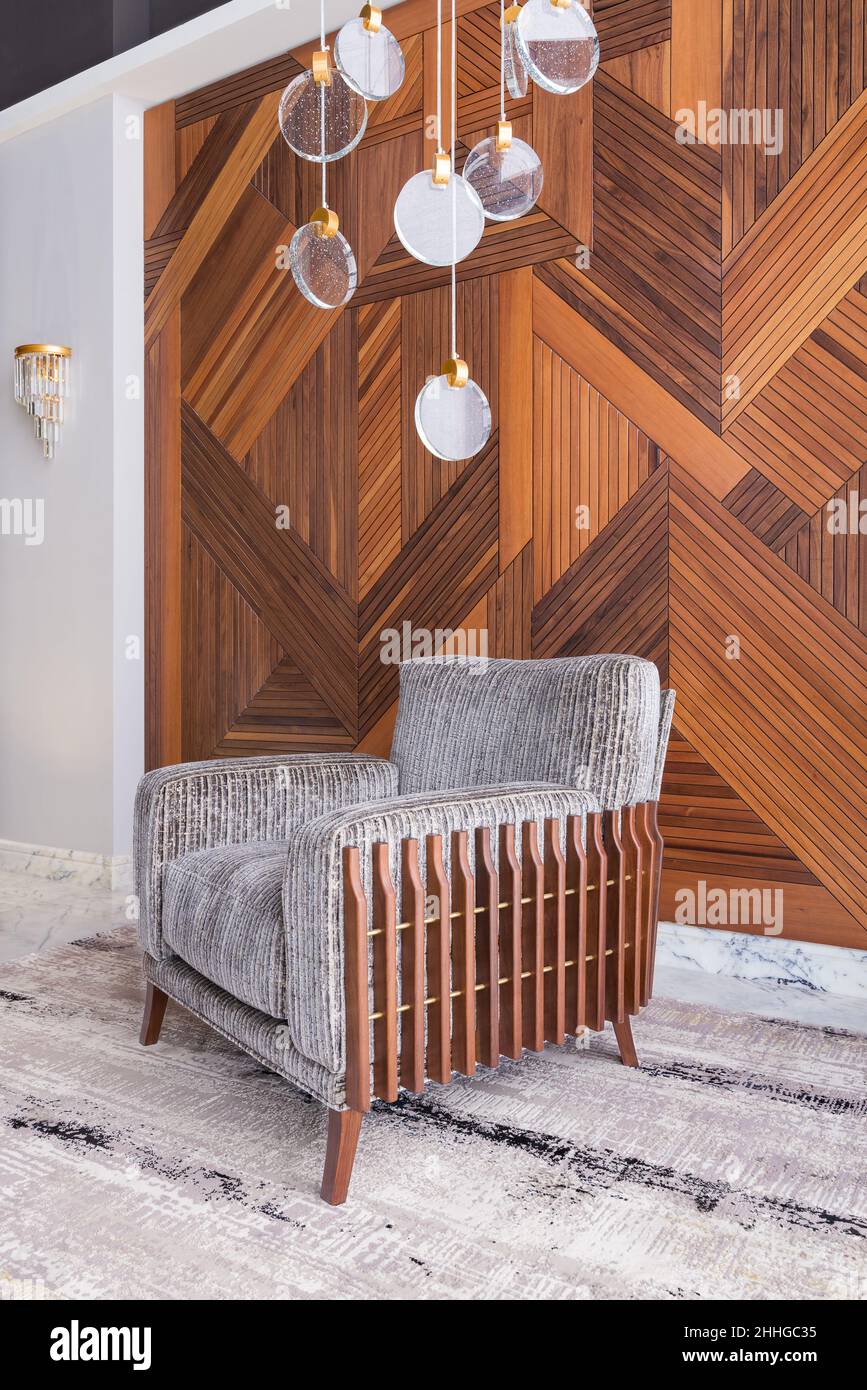 Moderno sillón gris, y una moderna araña de cristal, en un vestíbulo con paredes de revestimiento de madera decoradas, y alfombra moderna de color beige Foto de stock