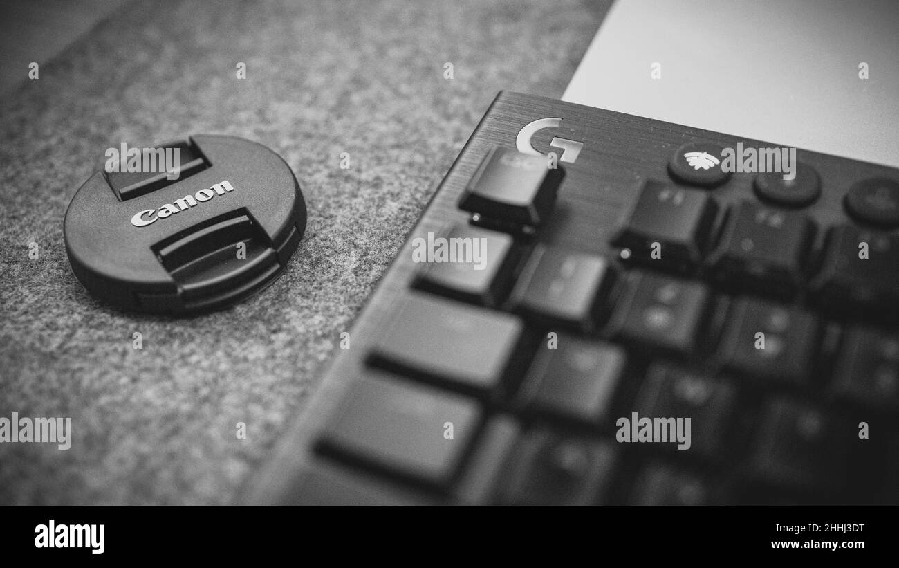 Escritorio con teclado parcialmente visible y tapa de lente canónica Foto de stock