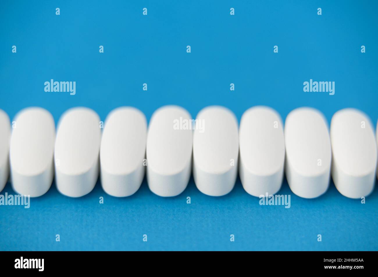 muchas píldoras blancas sobre fondo azul con espacio de copia Foto de stock