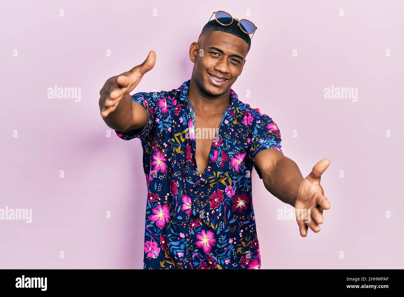 Hombre negro joven con camisa hawaiana y gafas de mirando la cámara sonriendo con los brazos abiertos para abrazar. Expresión alegre abrazando la felicidad Fotografía de stock - Alamy