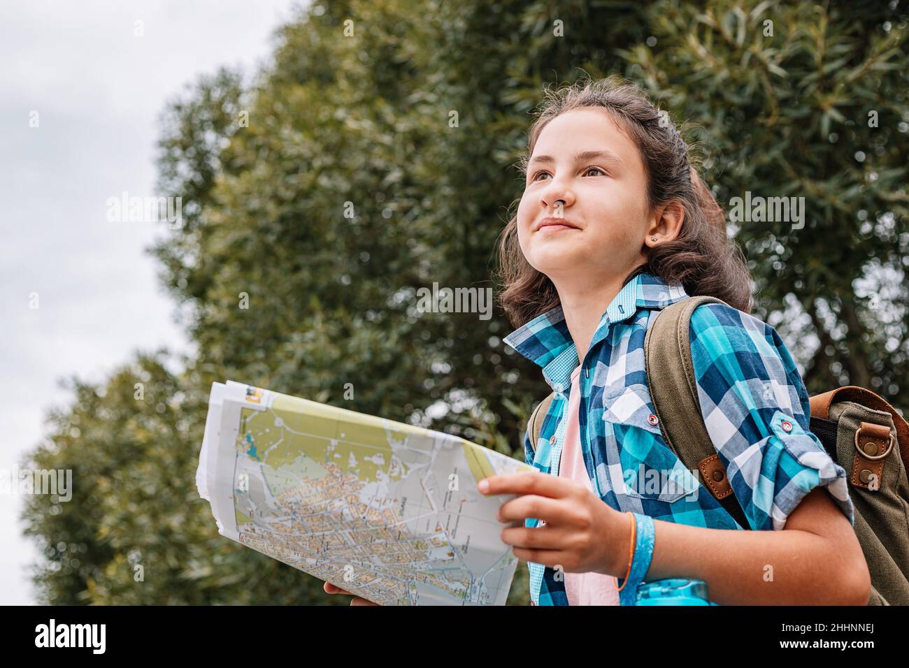 Una chica adolescente linda viaja en vacaciones de verano. Hipster niña con  una mochila mira un mapa de papel. Explorer en una excursión, viajando por  los lugares de interés de la ciudad