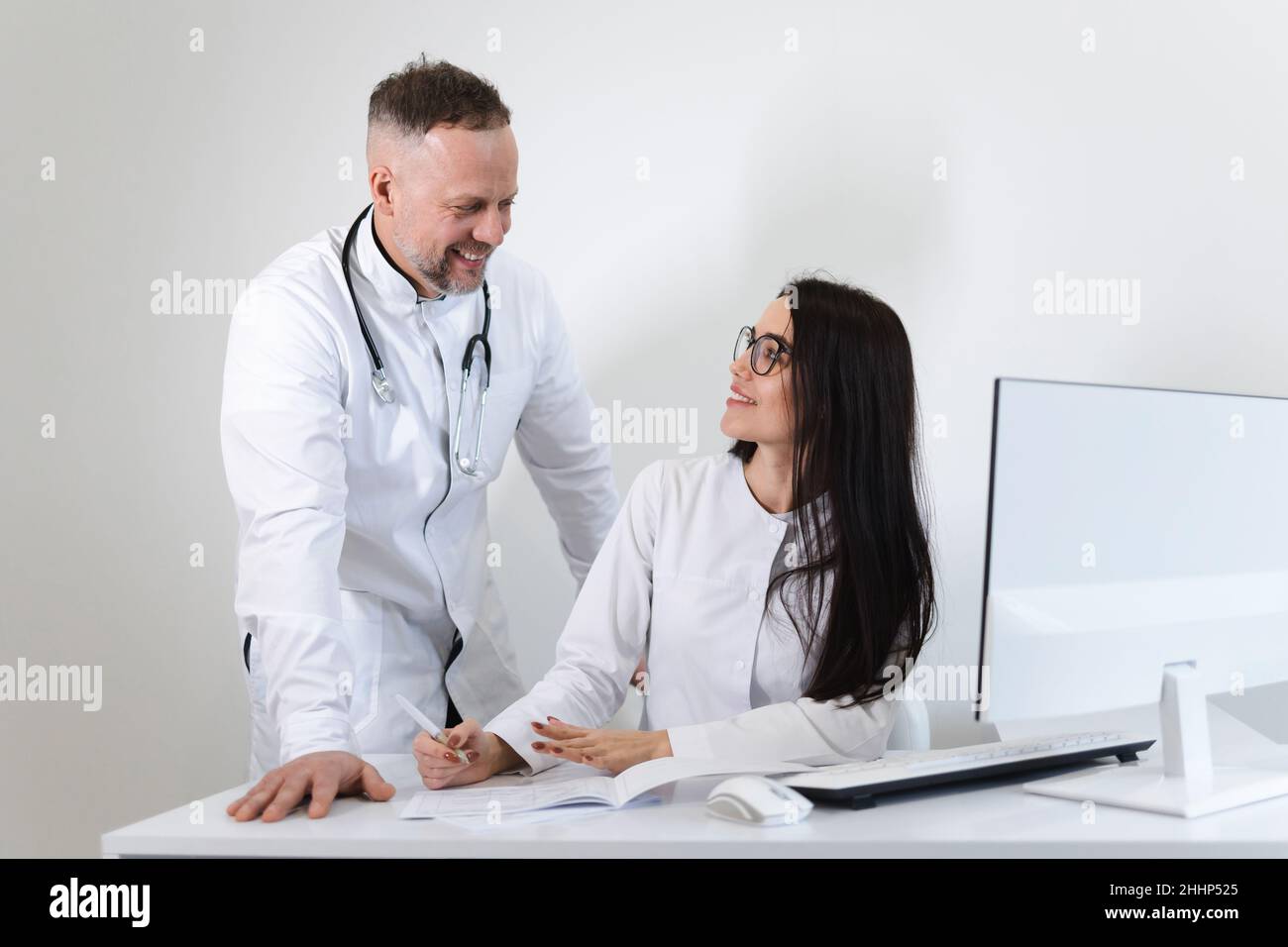 Una trabajadora médica joven consulta con el médico jefe masculino. Dos colegas médicos se divierten hablando en la oficina Foto de stock