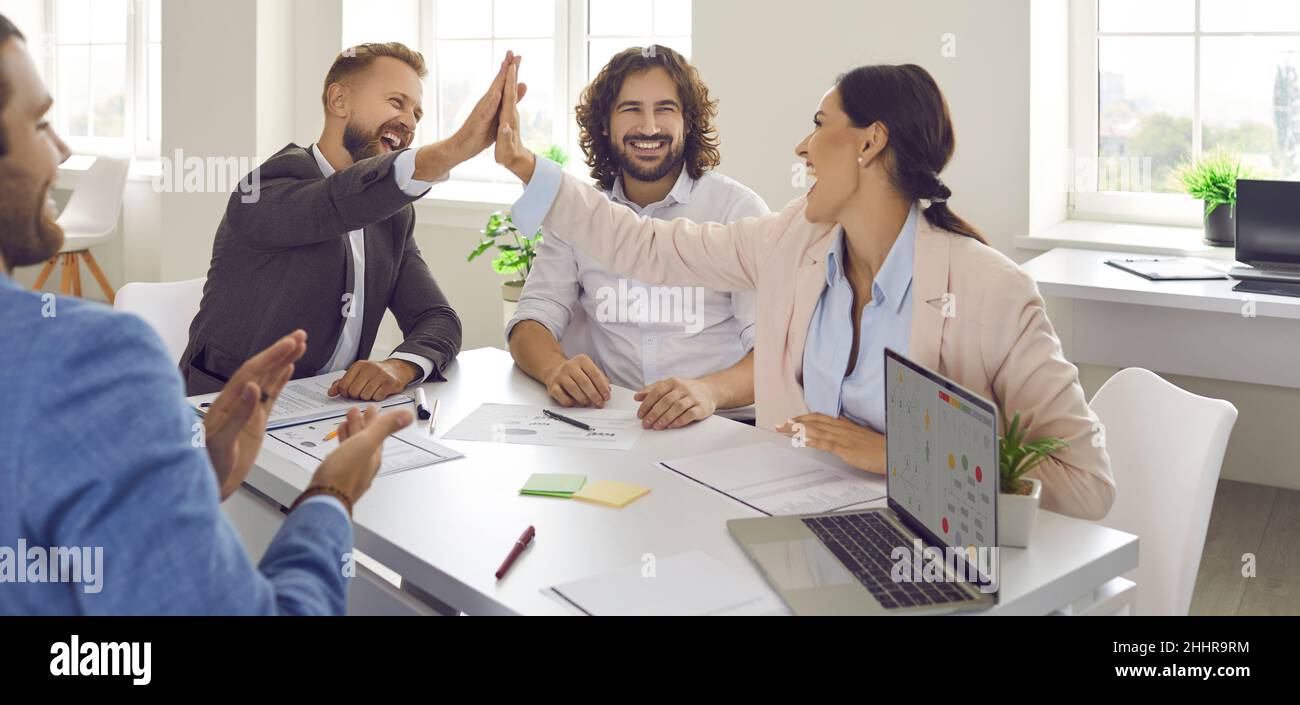 Los compañeros alegres y exitosos se dan cinco para un buen trabajo durante la reunión de negocios. Foto de stock