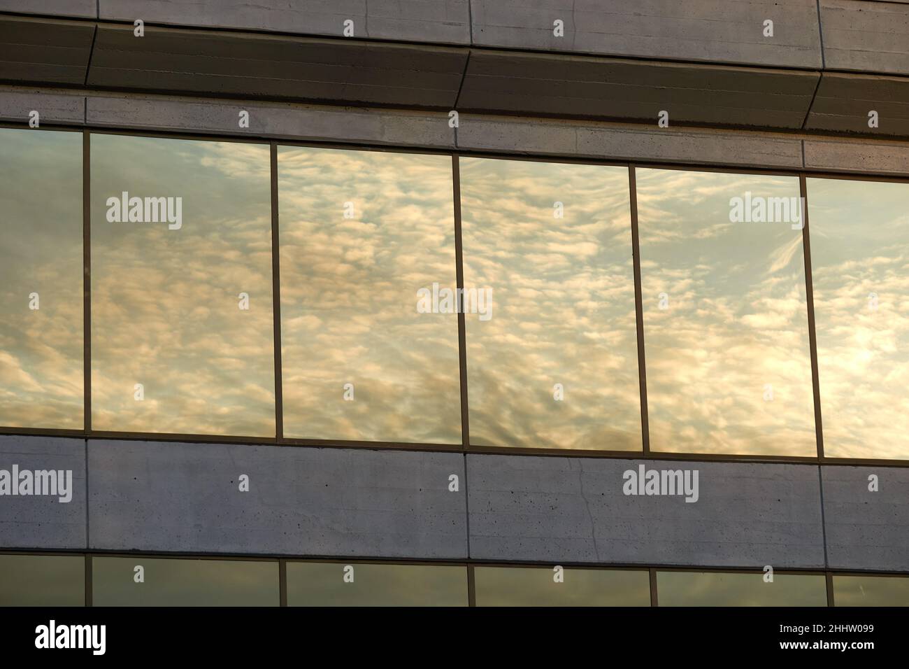 Las nubes blancas y el cielo se reflejan en las ventanas de un moderno edificio de oficinas de hormigón Foto de stock