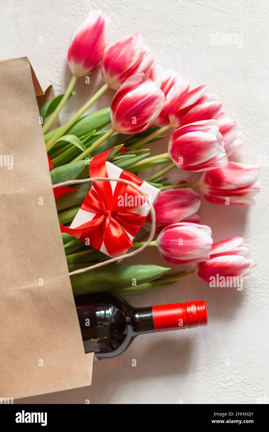 Día de la Madre o Día de la Mujer, cumpleaños, boda. Tulipanes de primavera  con una caja de regalo y una botella de vino en una bolsa de papel  Fotografía de stock -
