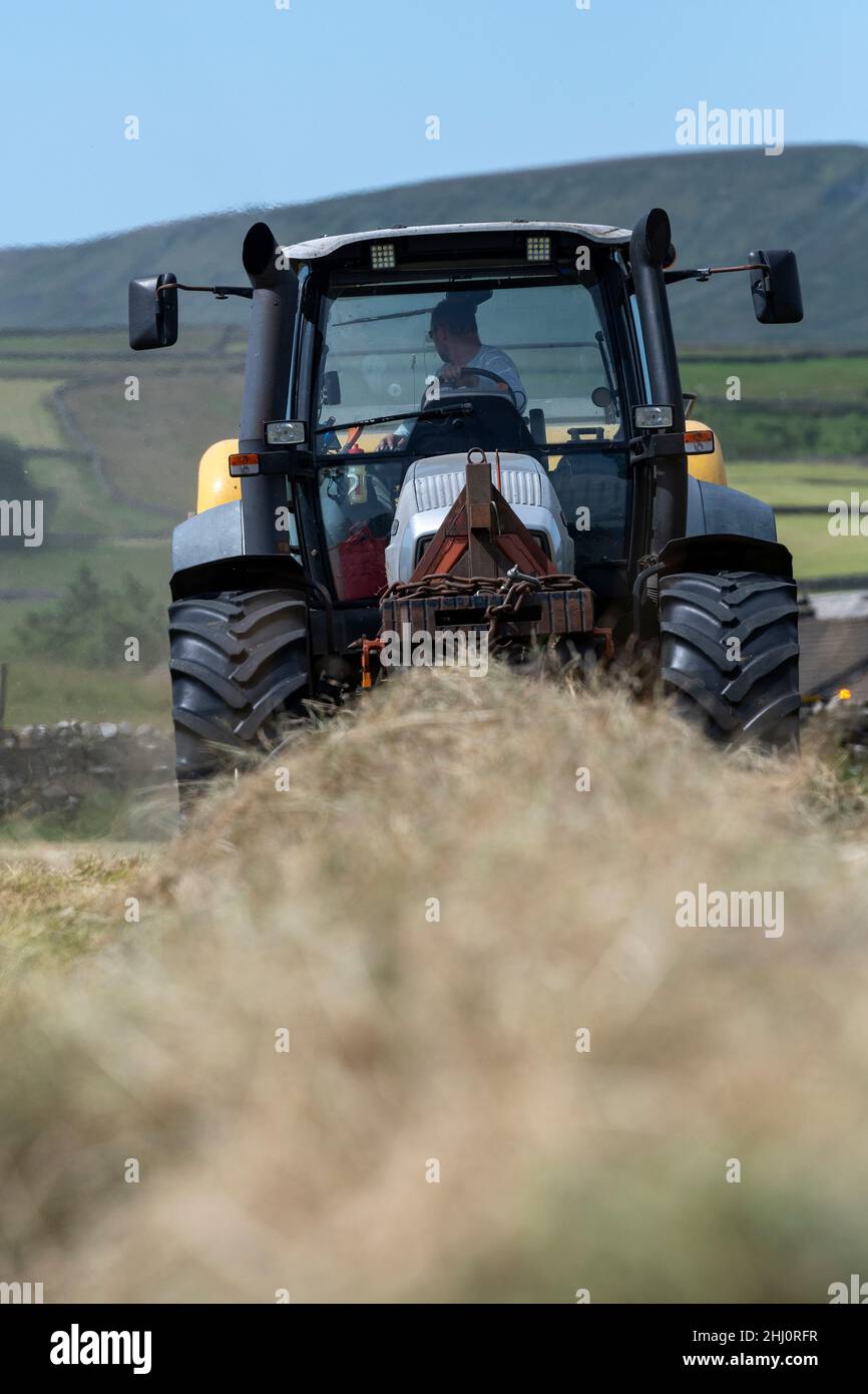Granjero que hace heno de prados de tierras altas tradicionales, con un  tractor Hurlimann XL y una empacadora cuadrada de alta densidad New Holland  BB9060. Hawes, North Yorkshire, U Fotografía de stock -