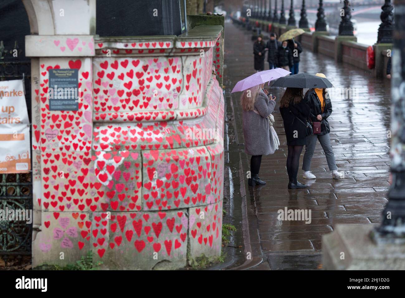 Los peatones son vistos de pie junto a corazones rojos, que representan a los que murieron de Covid-19, en el National Covid Memorial Wall en Londres. Foto de stock
