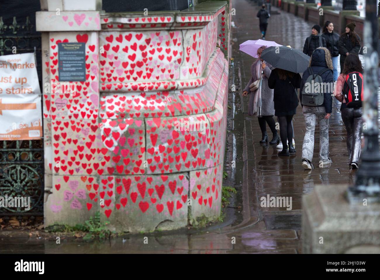 Los peatones son vistos de pie junto a corazones rojos, que representan a los que murieron de Covid-19, en el National Covid Memorial Wall en Londres. Foto de stock