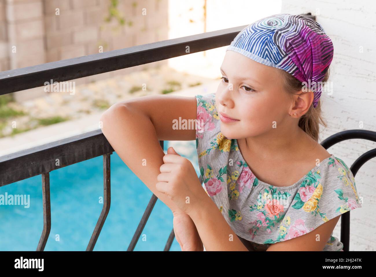 Niña europea con vistoso vestido y bandana se sienta en un balcón en un día  de verano, cerca de retrato al aire libre Fotografía de stock - Alamy