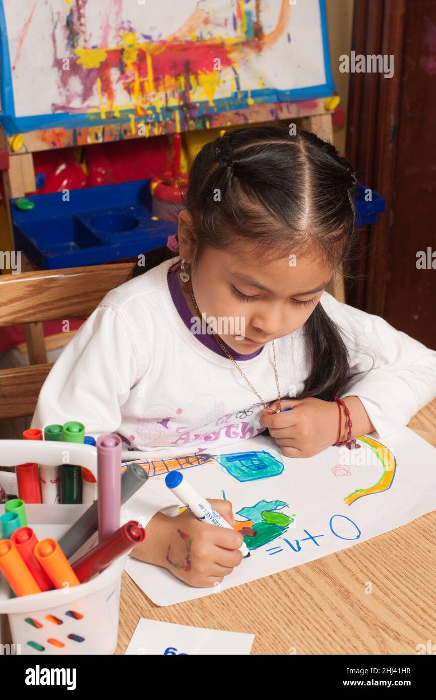 Educación Preescolar 4-5 años niña sentada en la mesa escribiendo ecuación matemática en su dibujo 0 + 1 = sosteniendo marcador con trípode agarrar Foto de stock