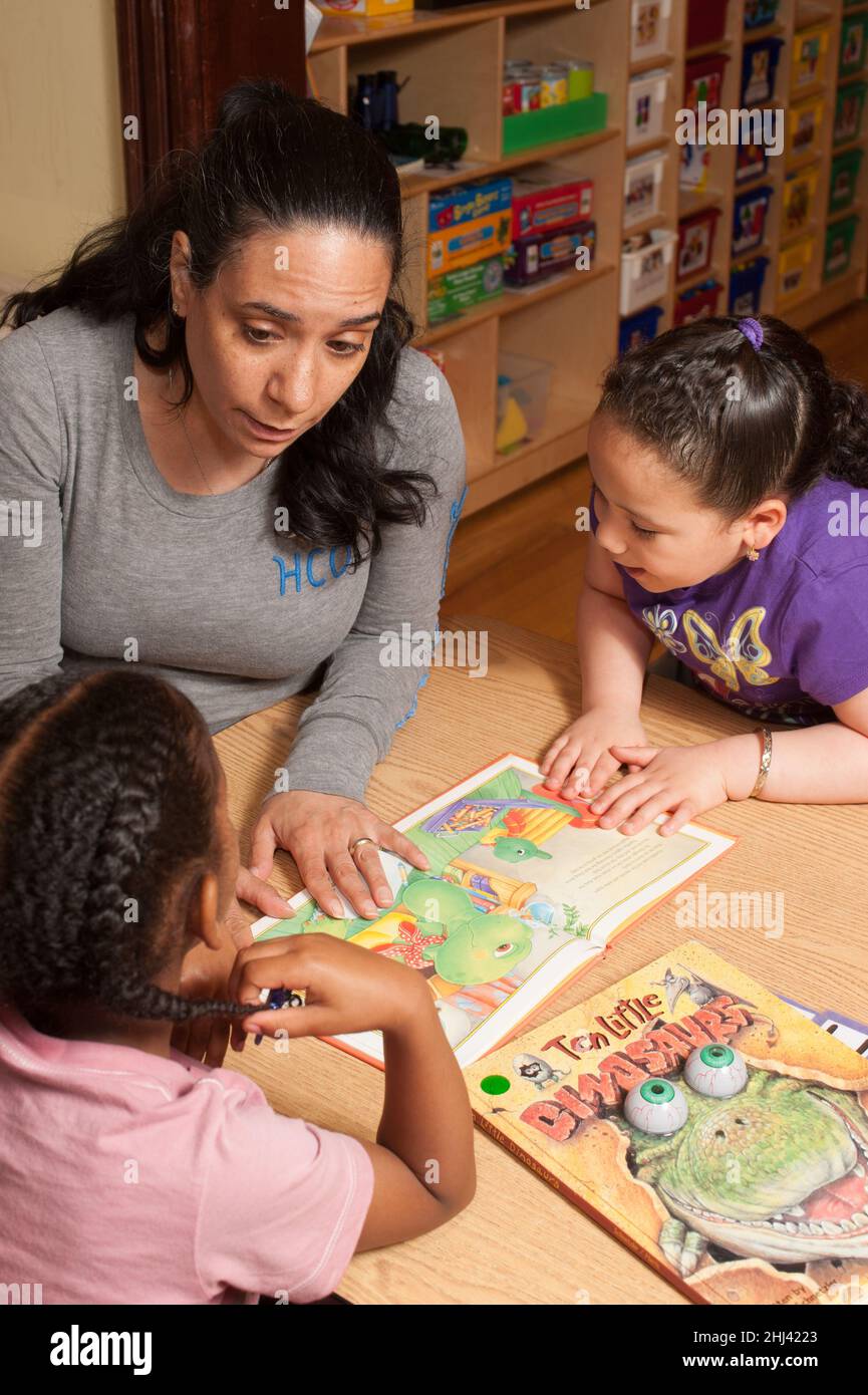 Educación Preescolar 3-4 años de edad maestra mujer leyendo libro de fotos a dos niñas y hablando con ellas sobre la historia Foto de stock