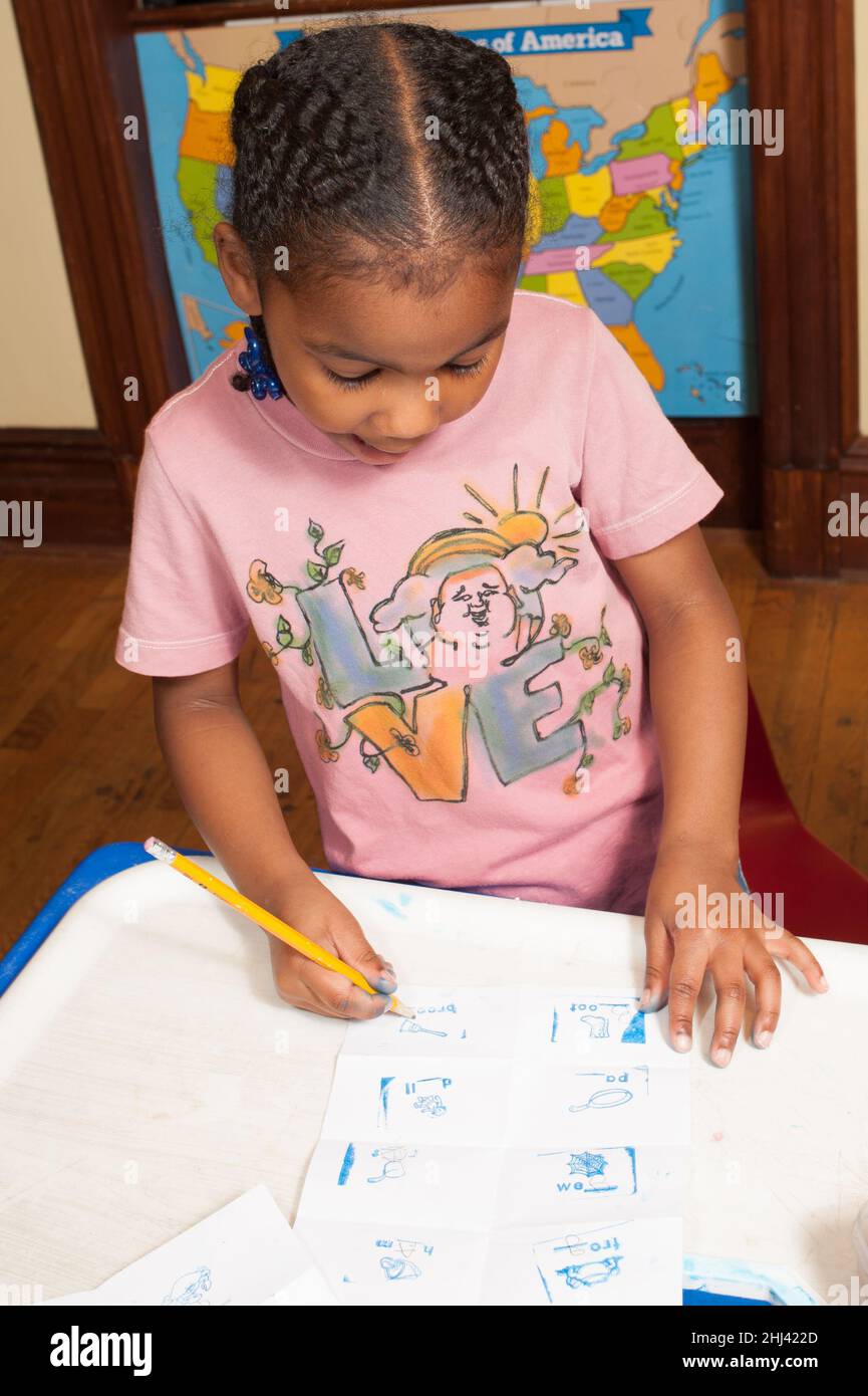 Educación Preescolar 4-5 años niña usando lápiz haciendo actividad sobre papel, sujetándola con trípode agarrar Foto de stock