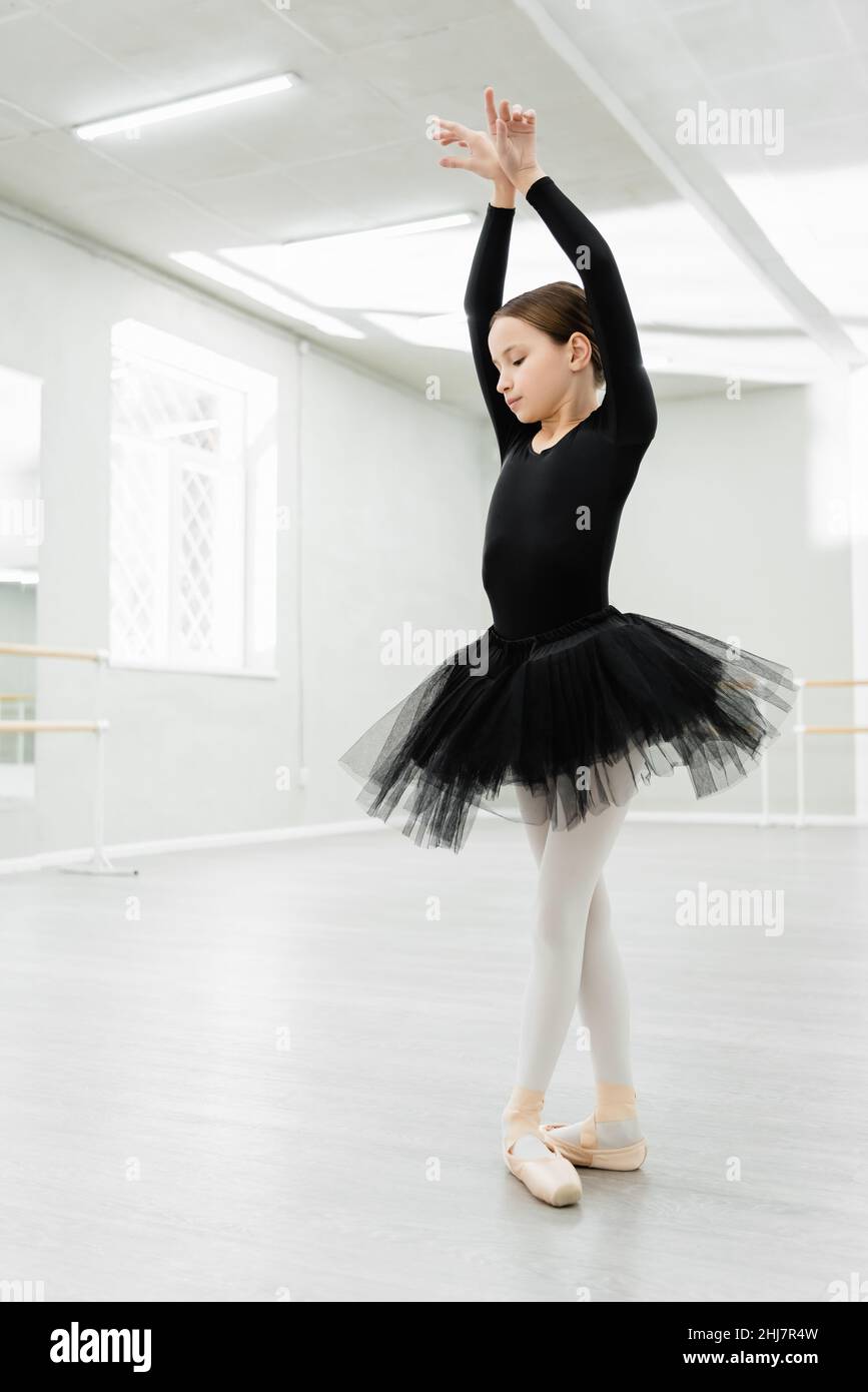 Pequeña bailarina con pelo en montón posando para la cámara niña en traje  negro medias blancas y zapatillas de punta entrenando en un estudio de  ballet