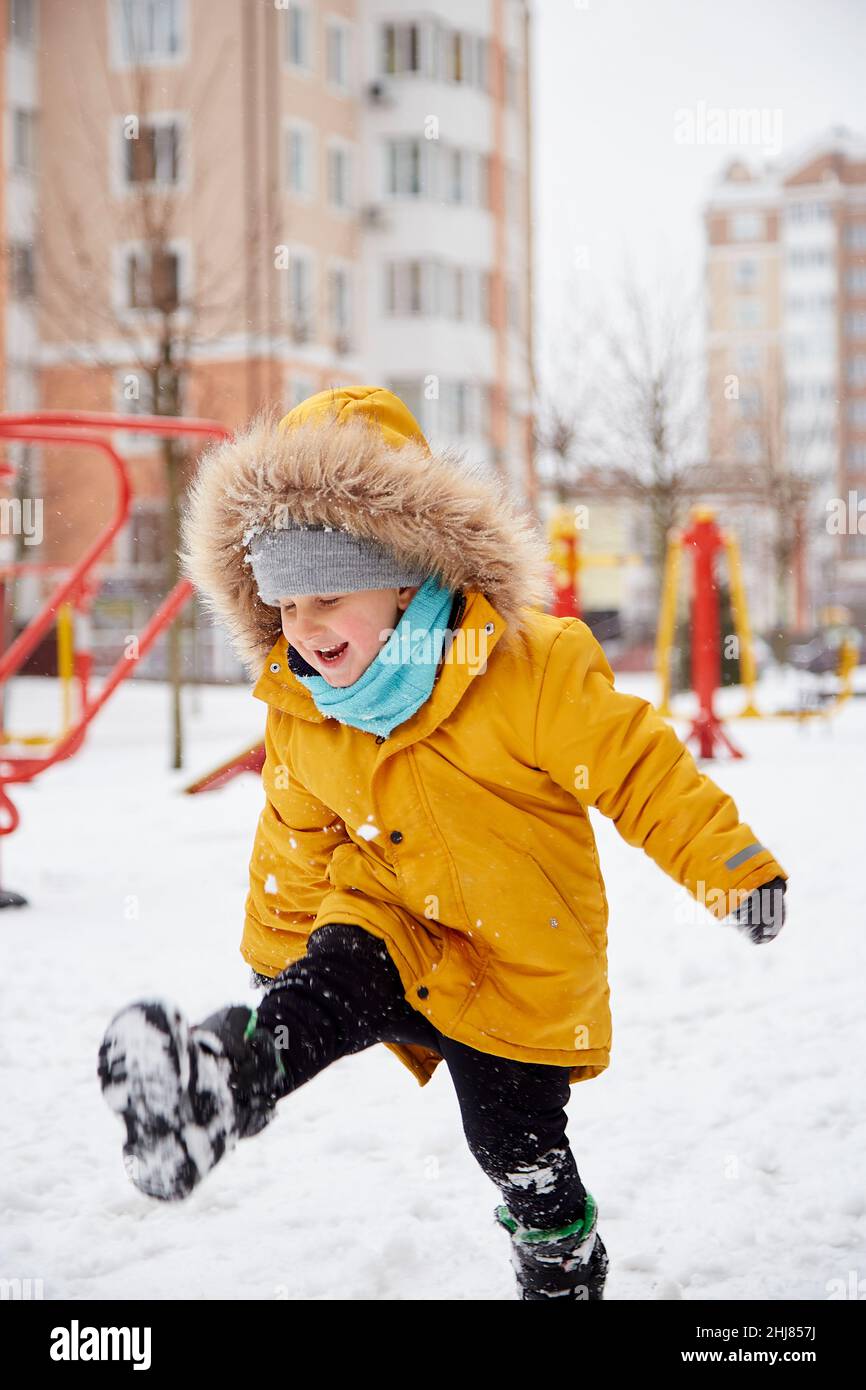 Un niño adorable disfrutando de la nieve en la ciudad. Diversión de invierno fuera. Niño en chaqueta de invierno naranja brillante. Fotografías de alta calidad Foto de stock