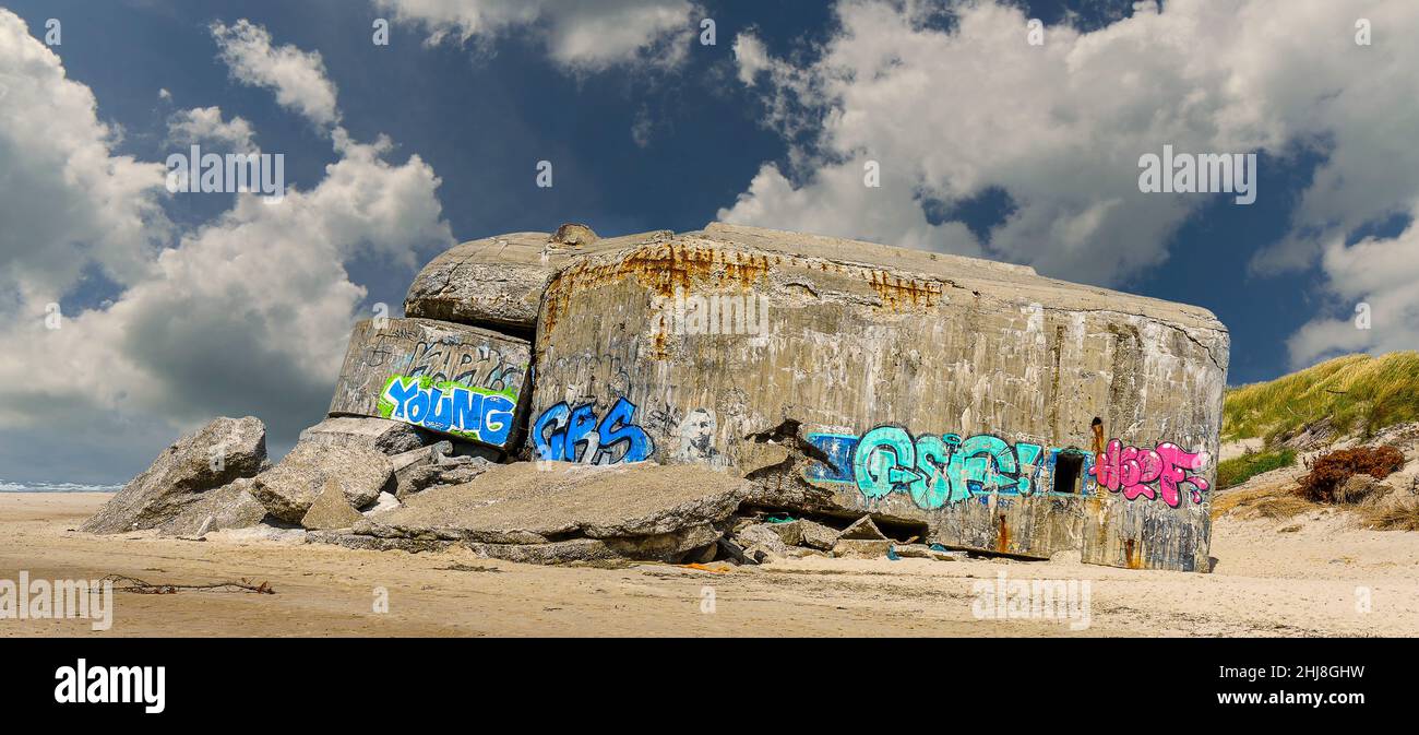 Ein zerstörter Bunker aus dem 2. Weltkrieg - bemalt mit Graffitis in hellblau und pink - an der dänischen Nordseeküste vor schönem Wolkenhimmel Foto de stock