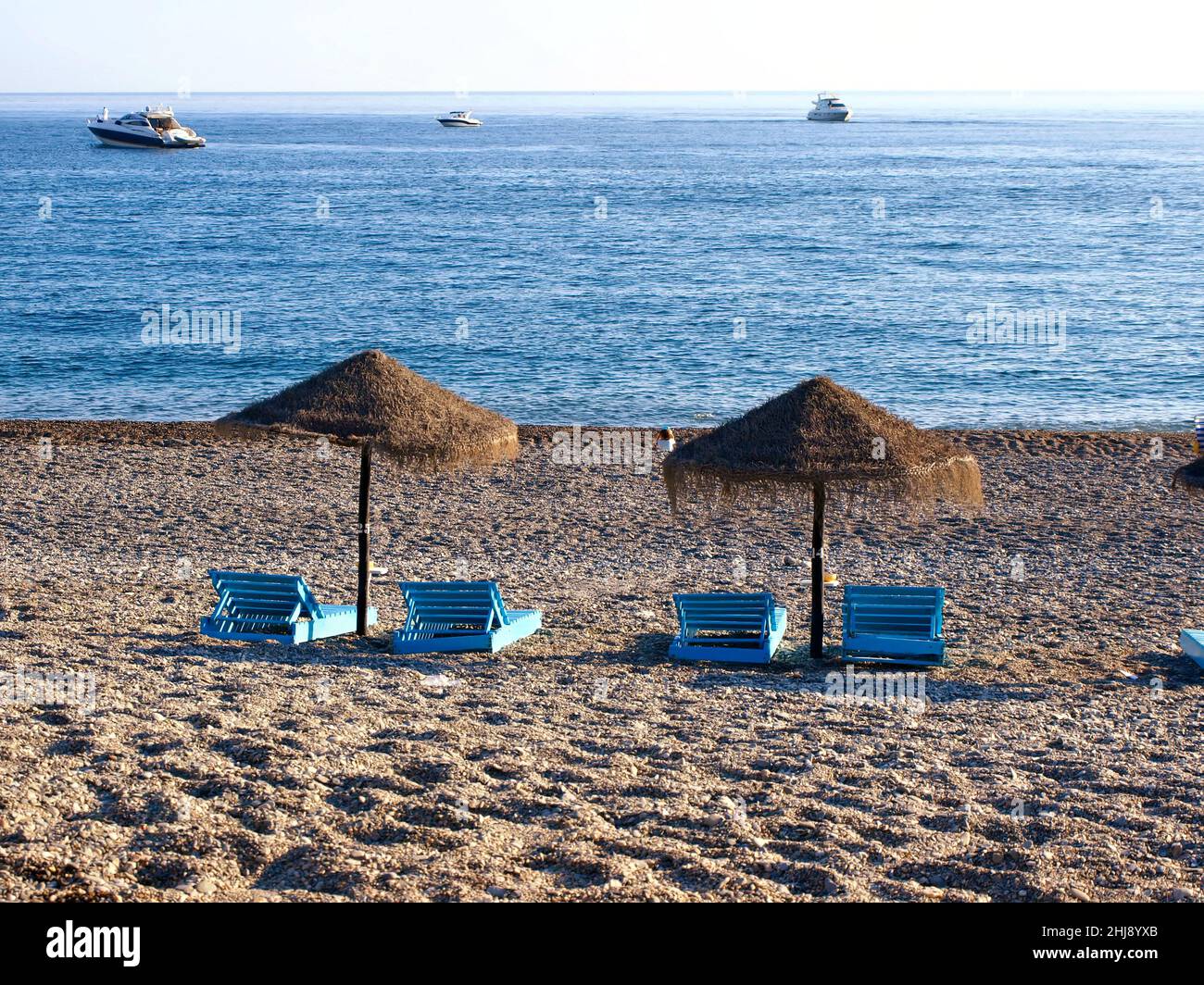 Relajante playa de ensueño con sombrillas de paja y tumbonas de madera en La Herradura, Almunecar, al sur de España, a última hora de la tarde. Foto de stock