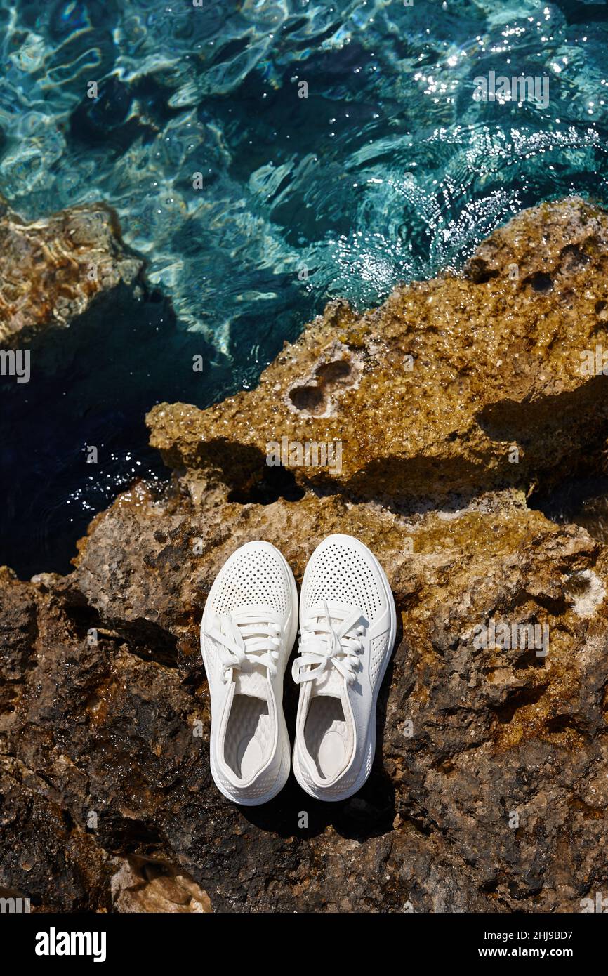 Zapatos de playa blancos universales sobre fondo de rocas afiladas Foto de stock