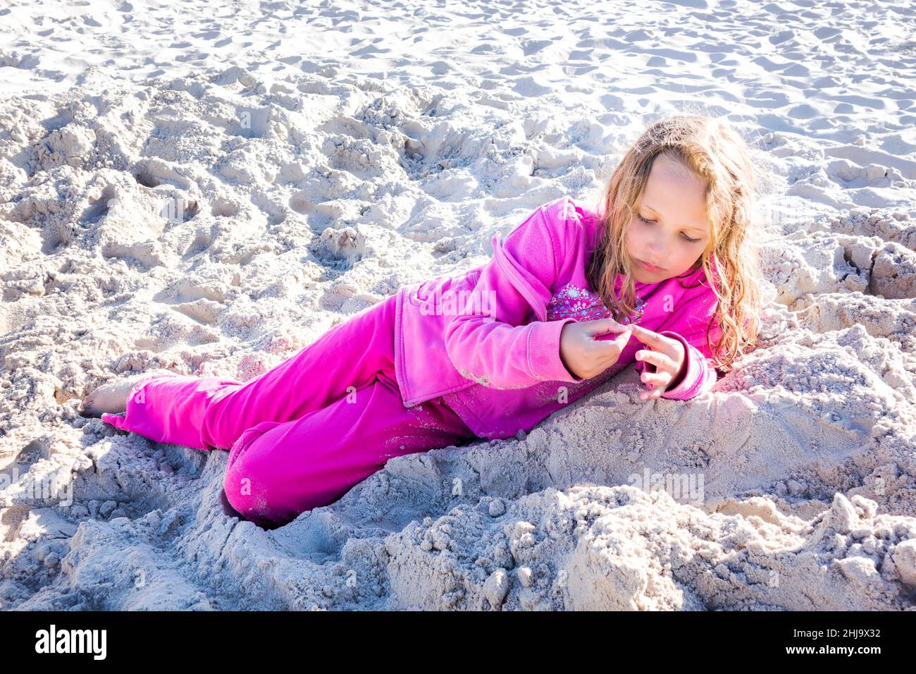 Una niña pensativa puesta en ropa rosa en la playa en arena durante el día  soleado Fotografía de stock - Alamy
