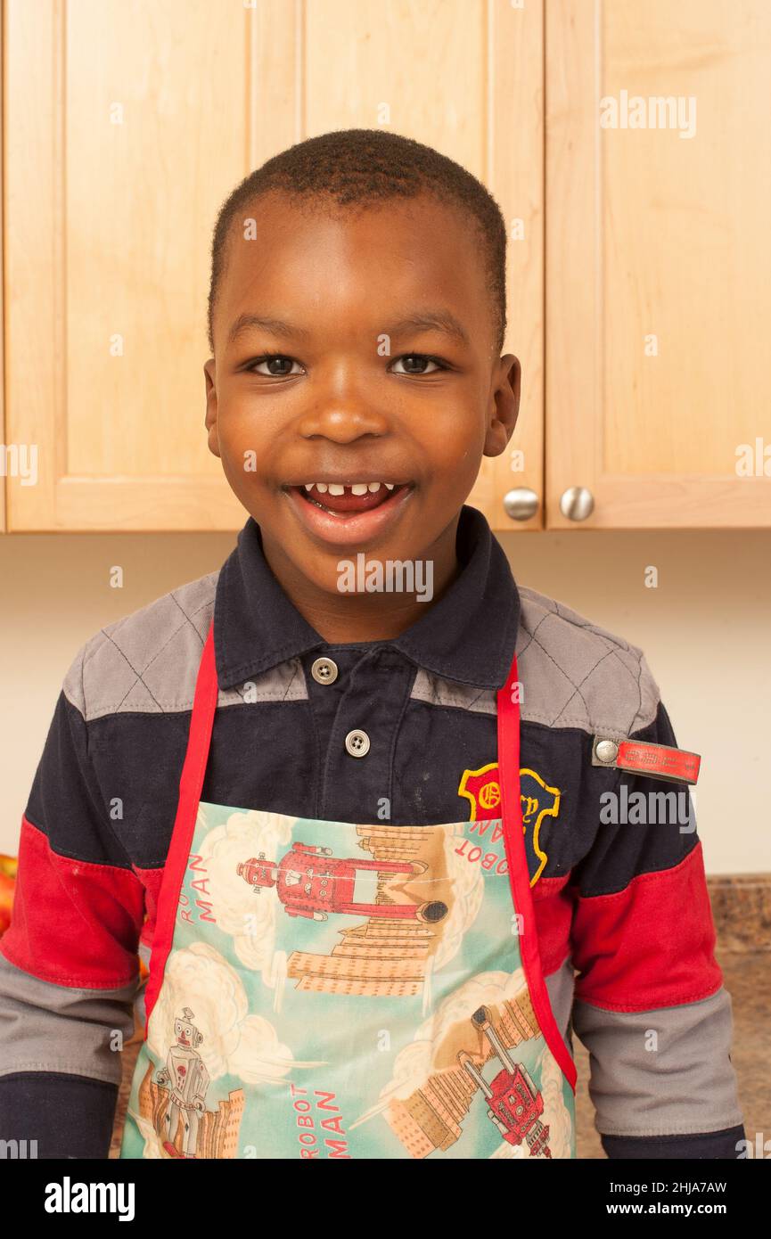 Feliz retrato de un niño de 4 años en la cocina con delantal Foto de stock