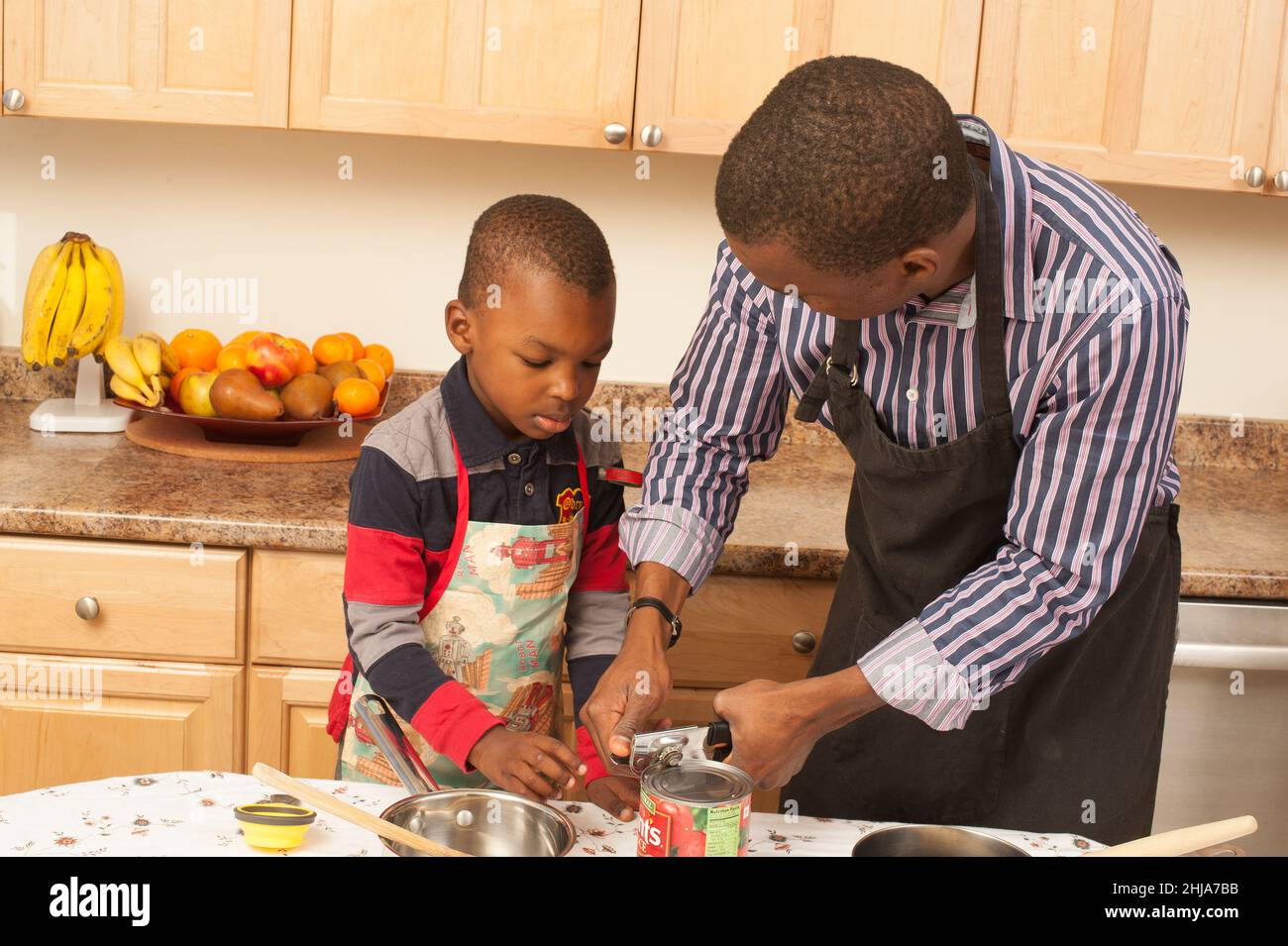 niño de 4 años en la cocina con el padre aprendiendo a usar el abrelatas para abrir la lata de tomates Foto de stock