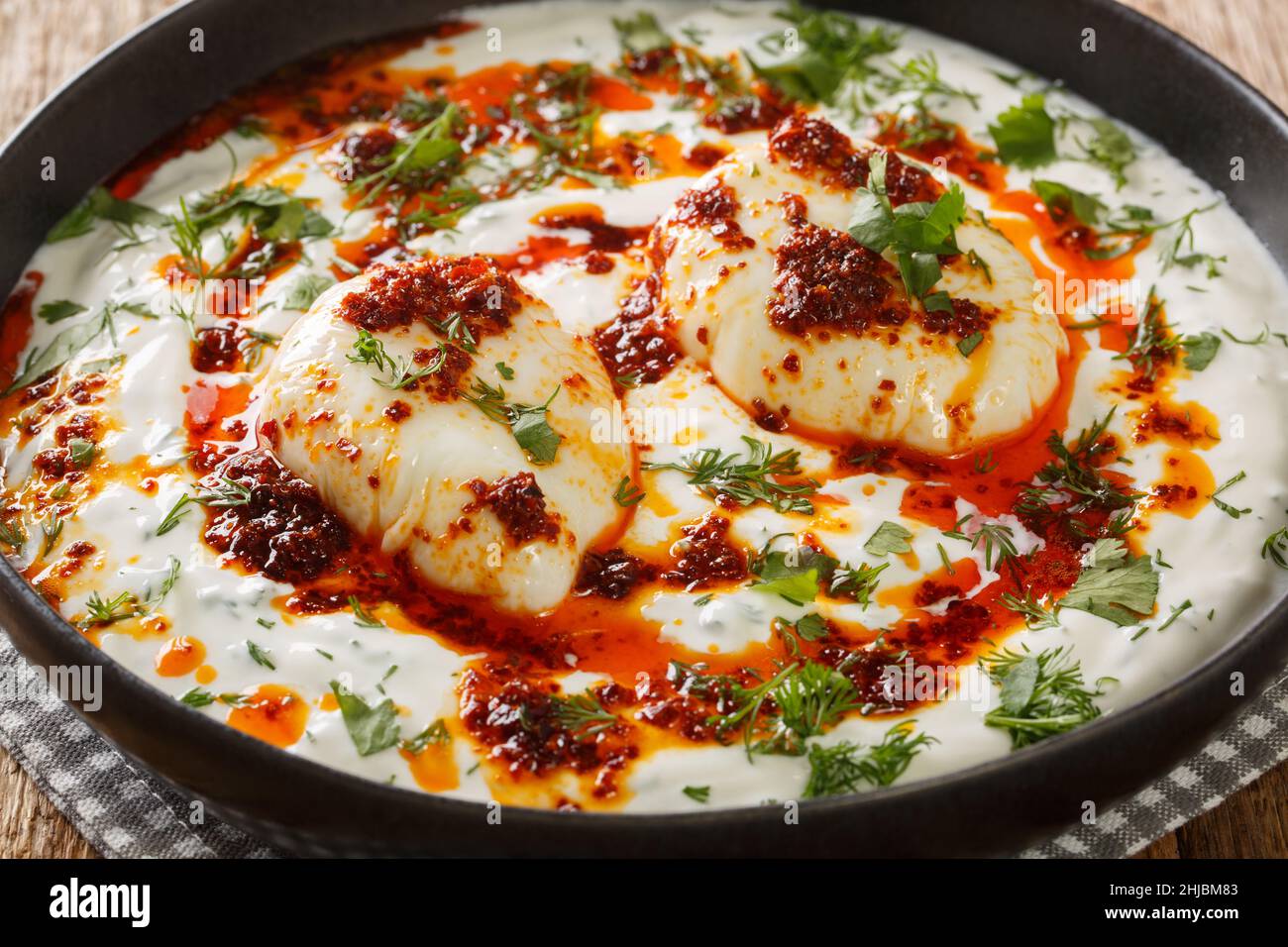 Desayuno turco sencillo y salado Cilbir es perfectamente escalfado huevos, servidos sobre un delicioso yogur con guarnición y mantequilla picante con hojuelas de pimiento rojo clos Foto de stock