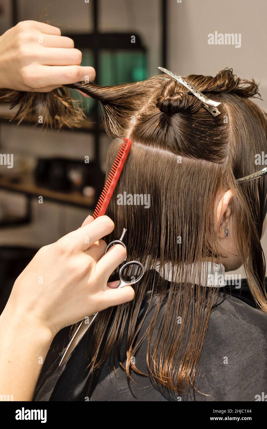Mano de peluquería haciendo corte de pelo de niño con clips de pelo en su  cabello en el salón. El Hairtician corta el pelo mojado del niño peinando  con el peine. Cliente
