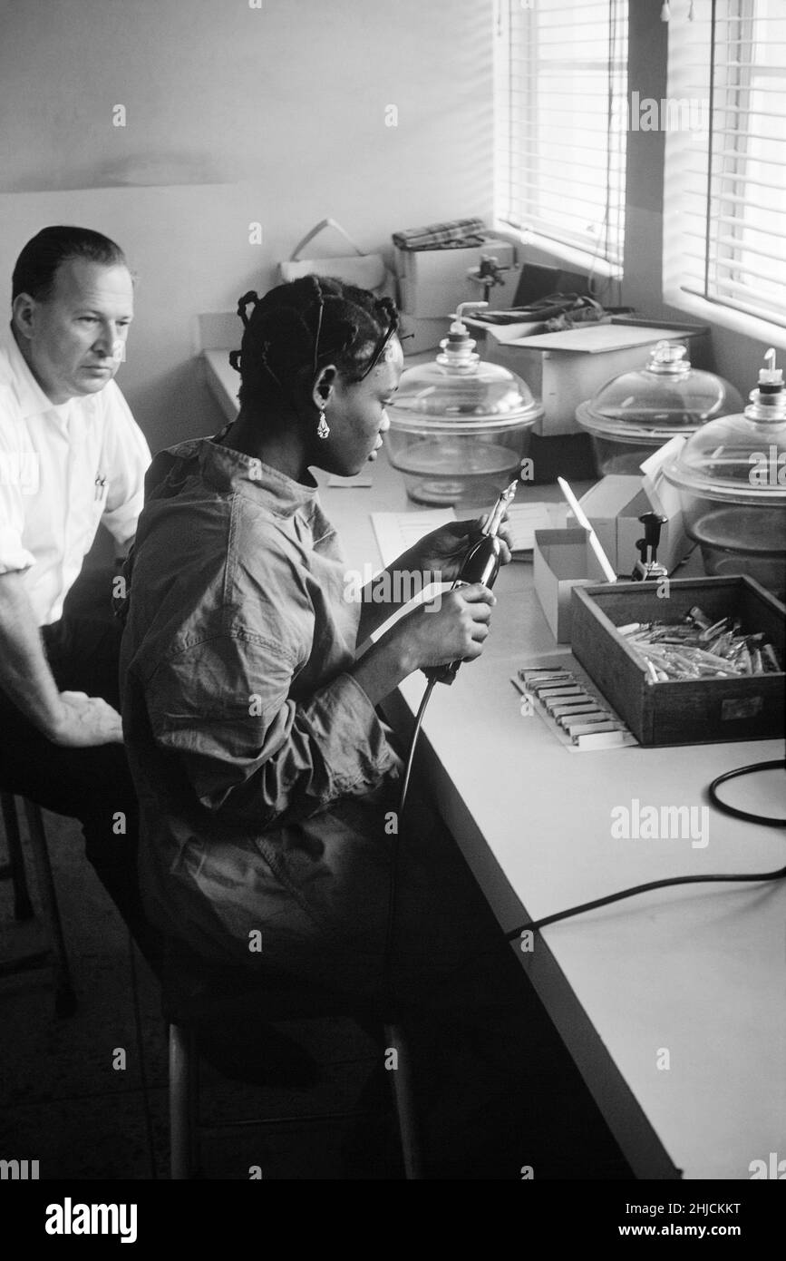 1967 John Noble, Jr., M.D. Esta fotografía de 1967 muestra el Programa de Erradicación de la Viruela, microbiólogo/virólogo, Nathaniel Rothstein sentado a la izquierda, mientras observaba a un técnico de laboratorio, mientras estaba probando viales de vacuna de viruela recién procesados, que contenían vacunas recién procesadas liofilizadas o liofilizadas. Este laboratorio se localizó en un suburbio de Lagos, Nigeria conocido como Yaba, durante la campaña de inmunización contra la viruela de ese país en 1960s y 1970s. Los brotes de viruela se han producido de vez en cuando durante miles de años, pero la enfermedad se ha erradicado después de un éxito Foto de stock