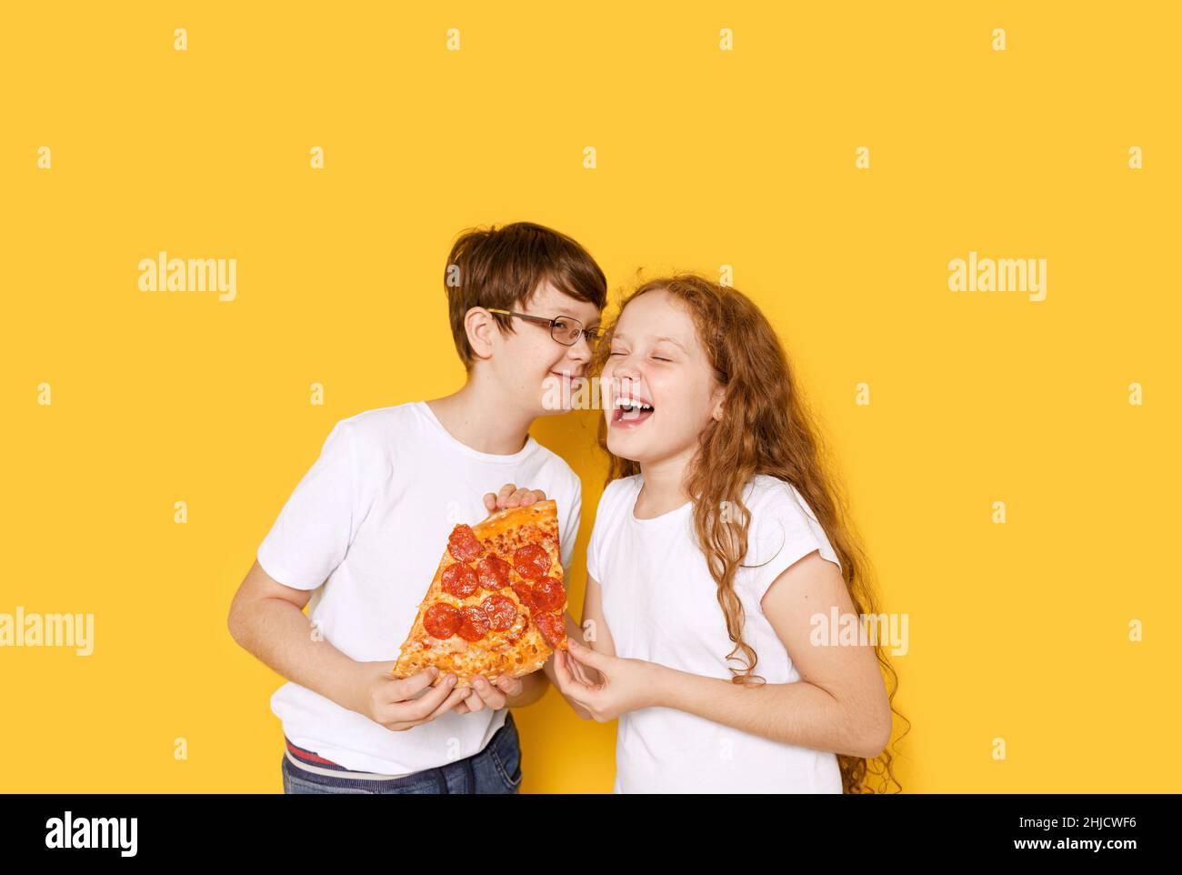 Chico y chica gracioso con pizza pepperoni sobre fondo amarillo. Feliz concepto de sonrisa saludable. Foto de stock