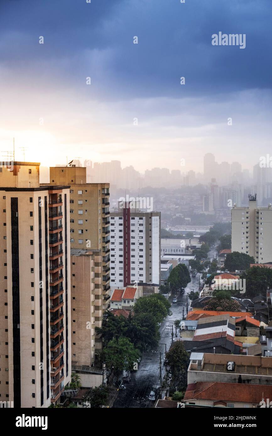 Bloques de apartamentos residenciales y viviendas de baja altura. Calle húmeda con lluvia. Cielo dramático con sol y nubes de lluvia oscura. São Paulo, Brasil Foto de stock