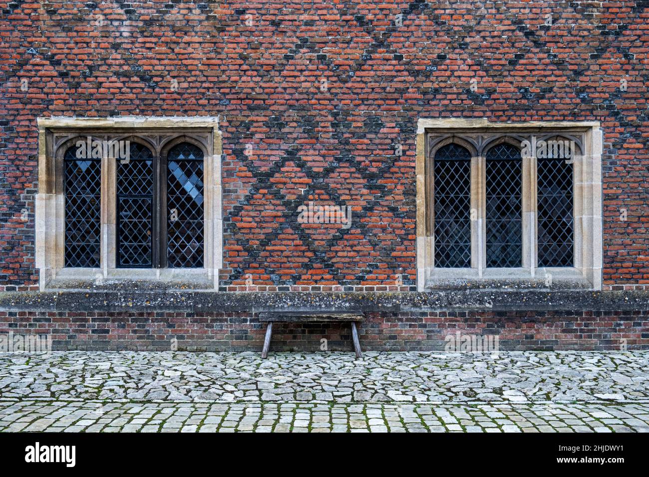 Ventanas de casamiento Tudor y ladrillo policromático Tudor Temprano: Ladrillos naranja-rojos en la Cruz-enlace Inglés. Jardín de adoquines. Hampton Court Palace, Londres Foto de stock