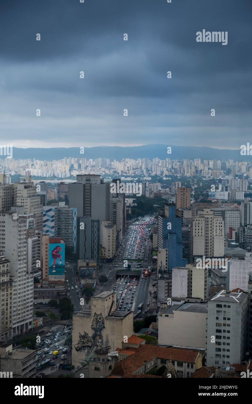 Brasil, São Paulo. Vista elevada del tráfico congestionado en la avenida Prestes Maia y de los edificios de gran altura, en el distrito del centro. Nubes gris oscuro llenas de humo. Foto de stock
