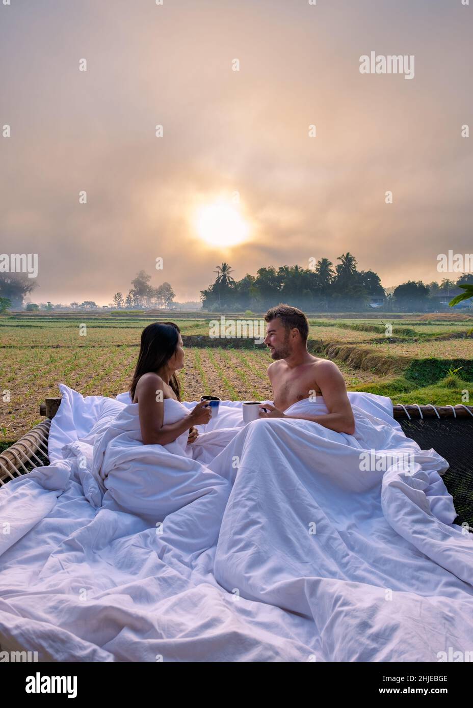 amanecer sobre arrozales en Nan Tailandia, hombre y mujer en la cama al  aire libre despertando con café por la mañana en Tailandia Nan. Romántico  amanecer en el dormitorio al aire libre