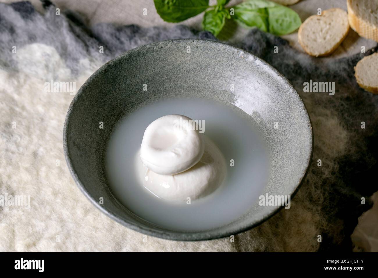 Queso tradicional italiano burrata anudado en un recipiente de cerámica gris sobre la mesa. Pan, aceitunas, verduras alrededor. Ingredientes para una cena mediterránea saludable. Foto de stock