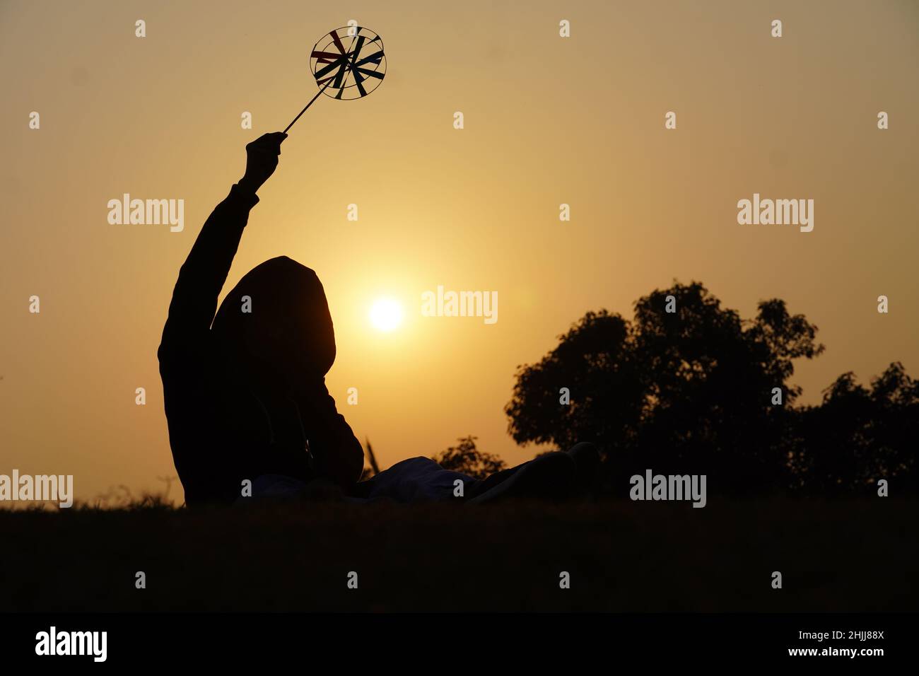 Feliz niño con un pétalo de juguete sobre un fondo de puesta de sol sobre un campo de trigo Foto de stock