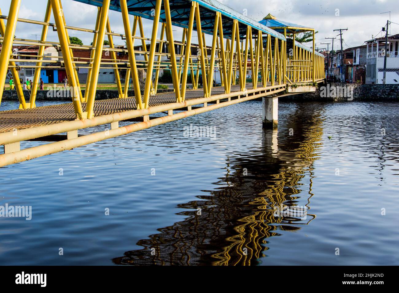 Pasarela peatonal de hierro sobre un río en colores amarillo y azul. Reflexión en el agua. Foto de stock