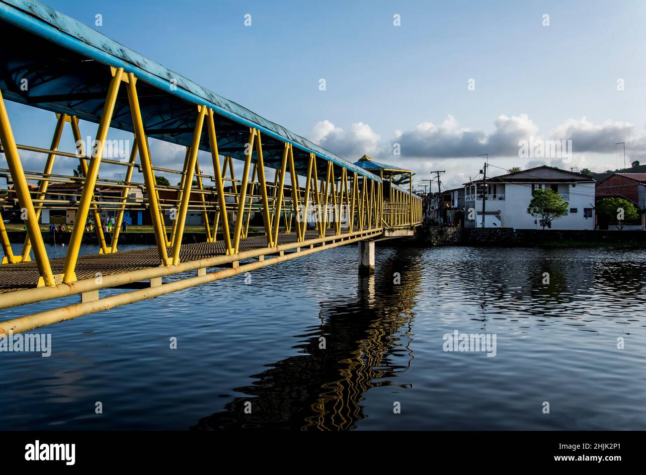 Pasarela peatonal de hierro sobre un río en colores amarillo y azul. Reflexión en el agua. Foto de stock