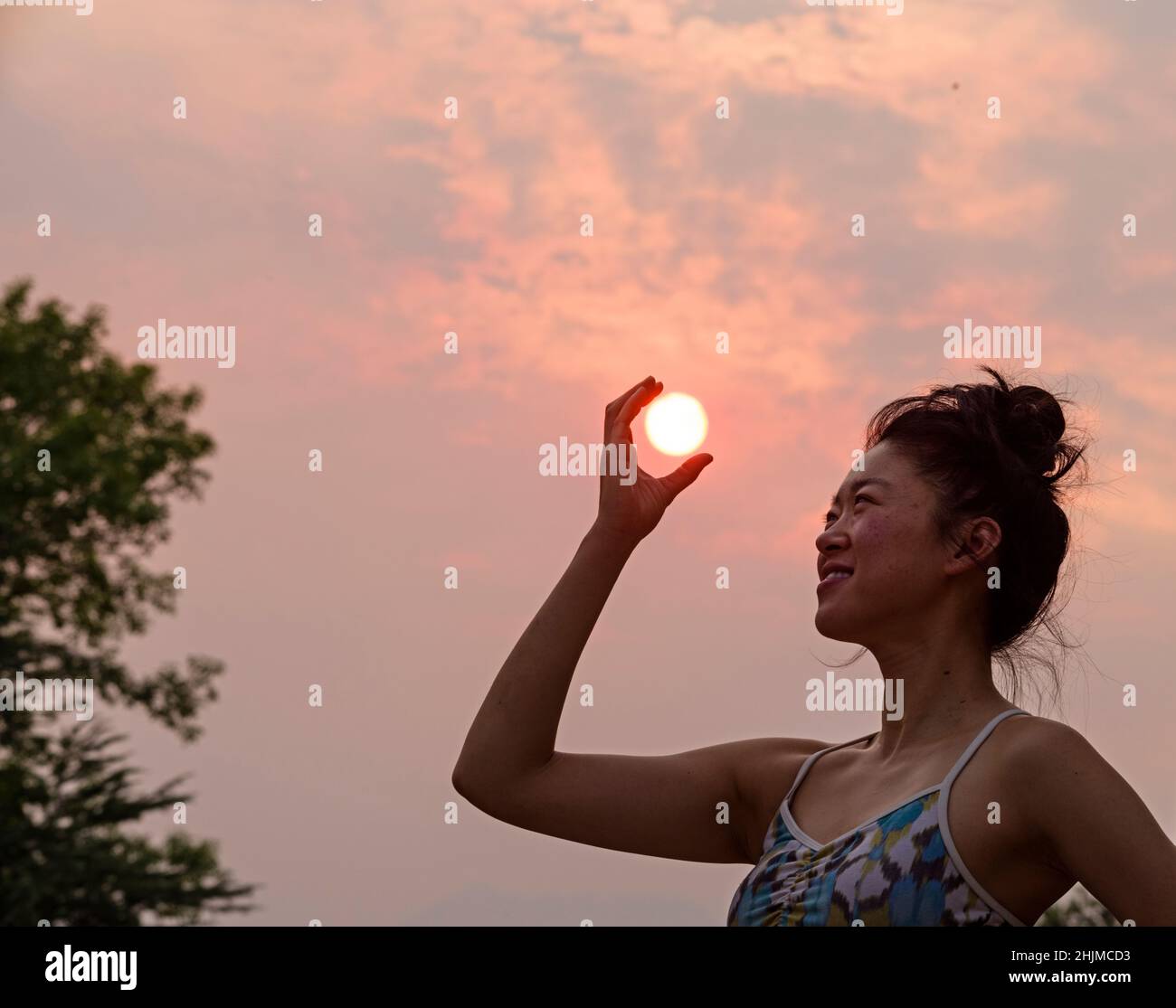 Mujer asiática sosteniendo el sol en un día con cielos ahumados Foto de stock