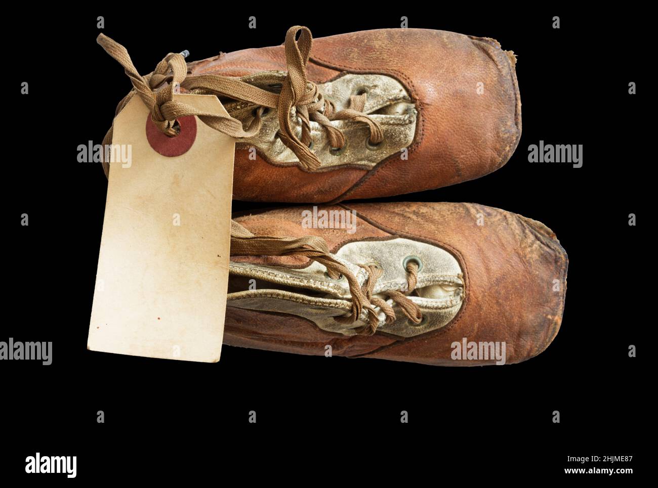 zapatos viejos de bebé de 1908 con una etiqueta de papel en blanco atada a los cordones sobre fondo negro Foto de stock
