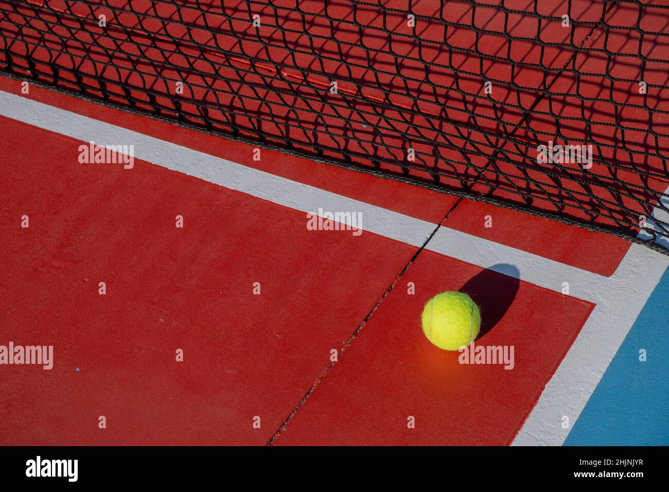 Pelota de tenis junto a la red de una cancha de tenis de superficie dura roja. Concepto deportivo de raqueta. Foto de stock