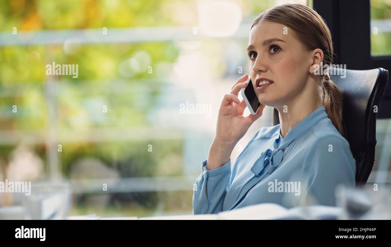 una mujer de negocios pensativa que se aleja mientras habla por teléfono móvil en la oficina Foto de stock