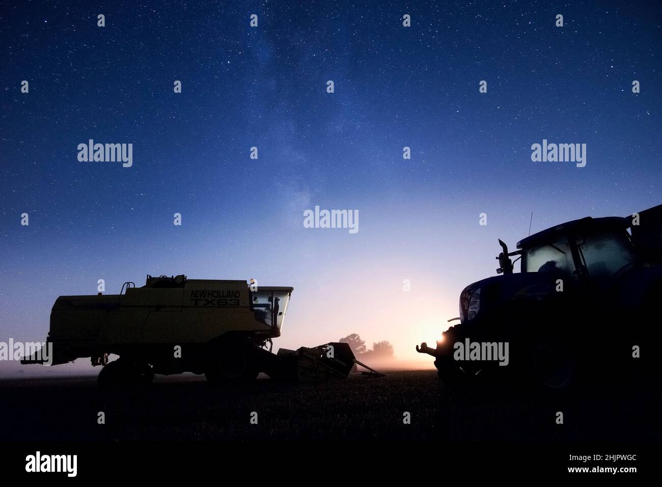 Cosechadora cosechadora y tractor por la noche con cielo estrellado y puesta de luna  Norfolk UK Foto de stock