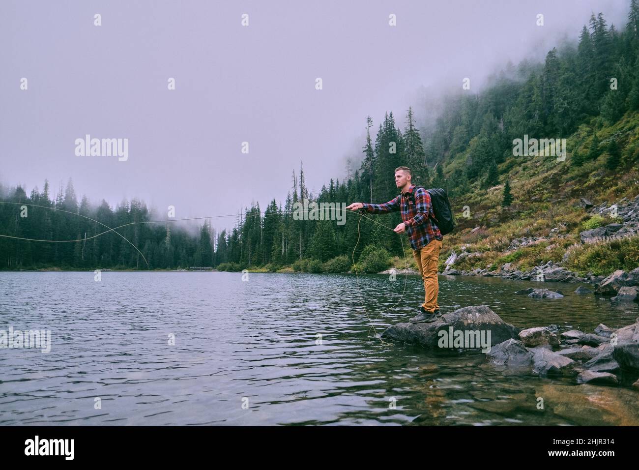 Un pescador de mosca parado en una roca hace un reparto en el lago 22. Foto de stock