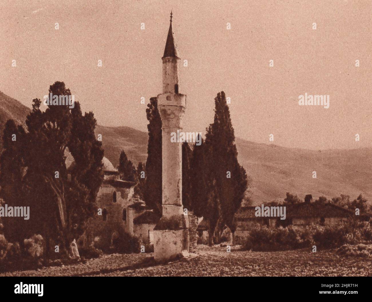 El esbelto minarete desafía a los altísimos cipreses que eclipsan a la pequeña mezquita en el bonito pueblo turco de Baba. Grecia (1923) Foto de stock