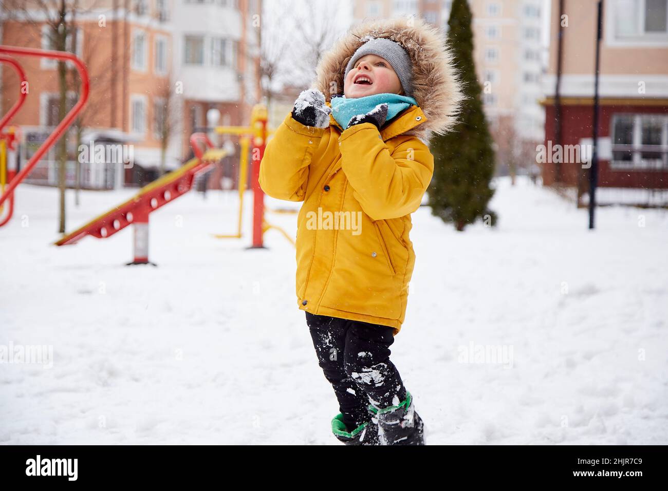 Feliz niño divertirse en la nieve en la ciudad. Diversión de invierno fuera. Niño en chaqueta de invierno naranja brillante. Fotografías de alta calidad Foto de stock