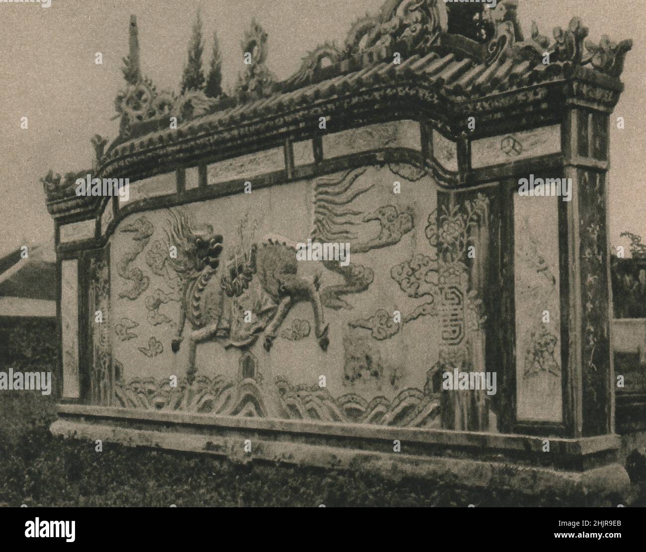 Este dragón que se inclina sobre una pantalla pintada en la semejanza de algunos toros elementales guarda un templo annamés en Hué. Vietnam (1923) Foto de stock