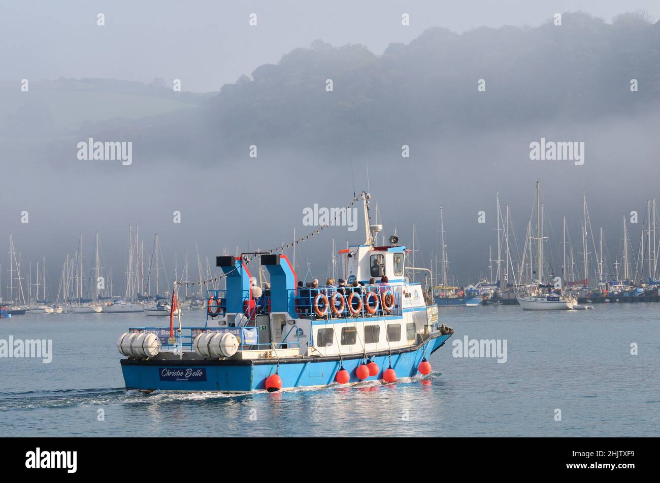 La gente a bordo de un ferry de pasajeros en el río Dart en una mañana tranquila y brumosa mientras el sol comienza a romper a través de la niebla. Dartmouth, Devon, Inglaterra, Reino Unido Foto de stock