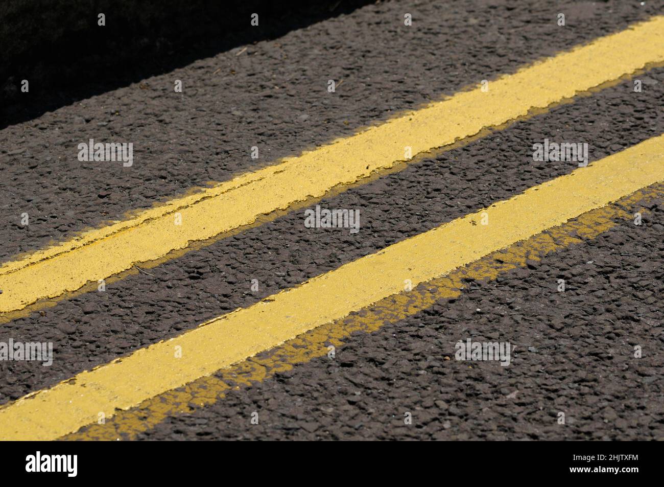 Primer plano de líneas amarillas dobles pintadas en la superficie de la carretera en una calle del Reino Unido que indica que no hay espera ni aparcamiento en ningún momento. Foto de stock